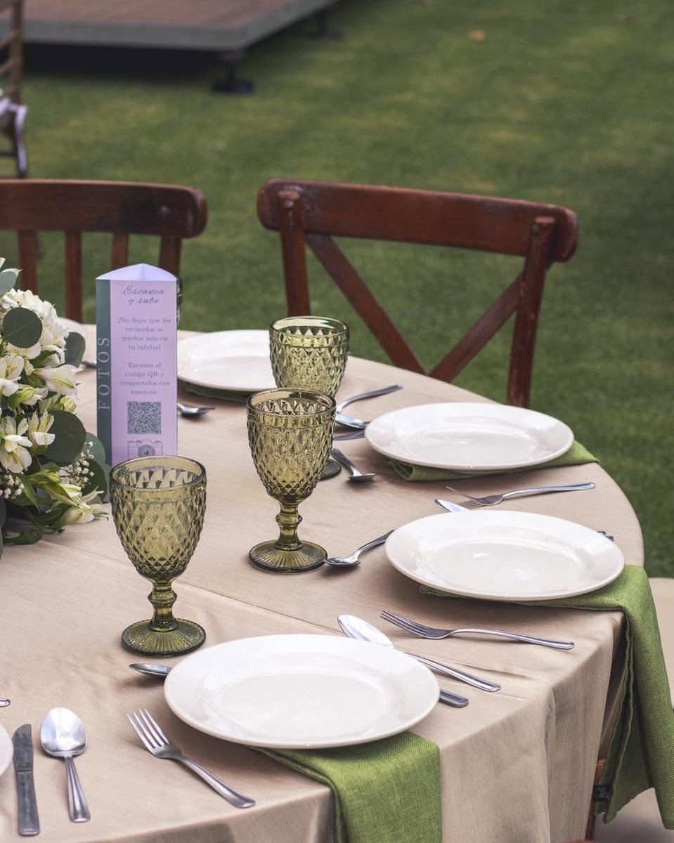 Mesa montada en el jardín con copas de cristal verde y flores