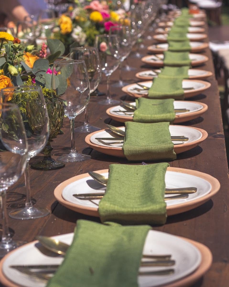 Detalle de mesa con servilletas verdes, platos de barro y cubiertos dorados
